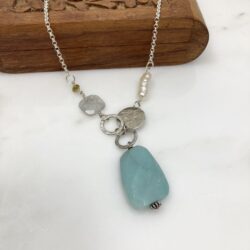 Faceted amazonite pendant with faceted square tourmaline, peridot, freshwater pearl and sterling accents on a sterling chain. The pendant is displayed on a small carved wooden box.