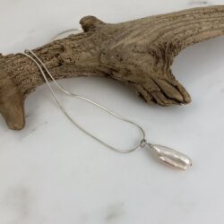 Pink biwa pearl solo pendant on a sterling snake chain. The chain is draped over a small piece of driftwood.