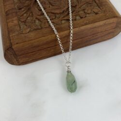 Seafoam green prehnite and sterling pendant displayed on a small carved wooden box. The stone is translucent with black quartz inclusions.