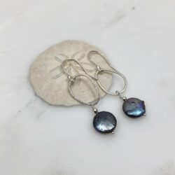 Purple-blue coin freshwater pearls and rounded triangle sterling loops on sterling ear wires. They're displayed on a sand dollar shell.