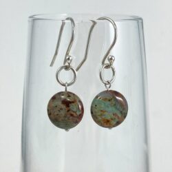 Puff coin rhyolite (rainforest jasper) earrings on sterling ear wires in shades of grey-green and browns. The earrings are displayed on a glass vessel.