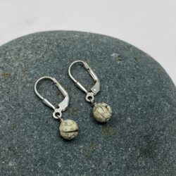 Creamy faceted silver leaf jasper with black accents on sterling leverback ear wires. They're displayed on a round grey beach stone.
