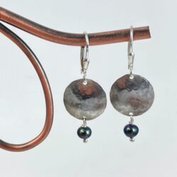 Circular sterling and purple freshwater pearl shield earrings displayed on decorative copper.