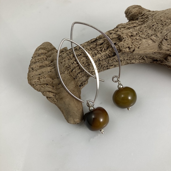 Yellow agate puff donut earrings on arch-shaped sterling ear hooks. They're displayed on a small piece of driftwood.